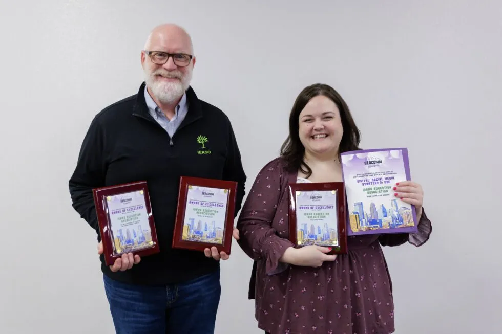 A smiling man and woman hold armfuls of awards