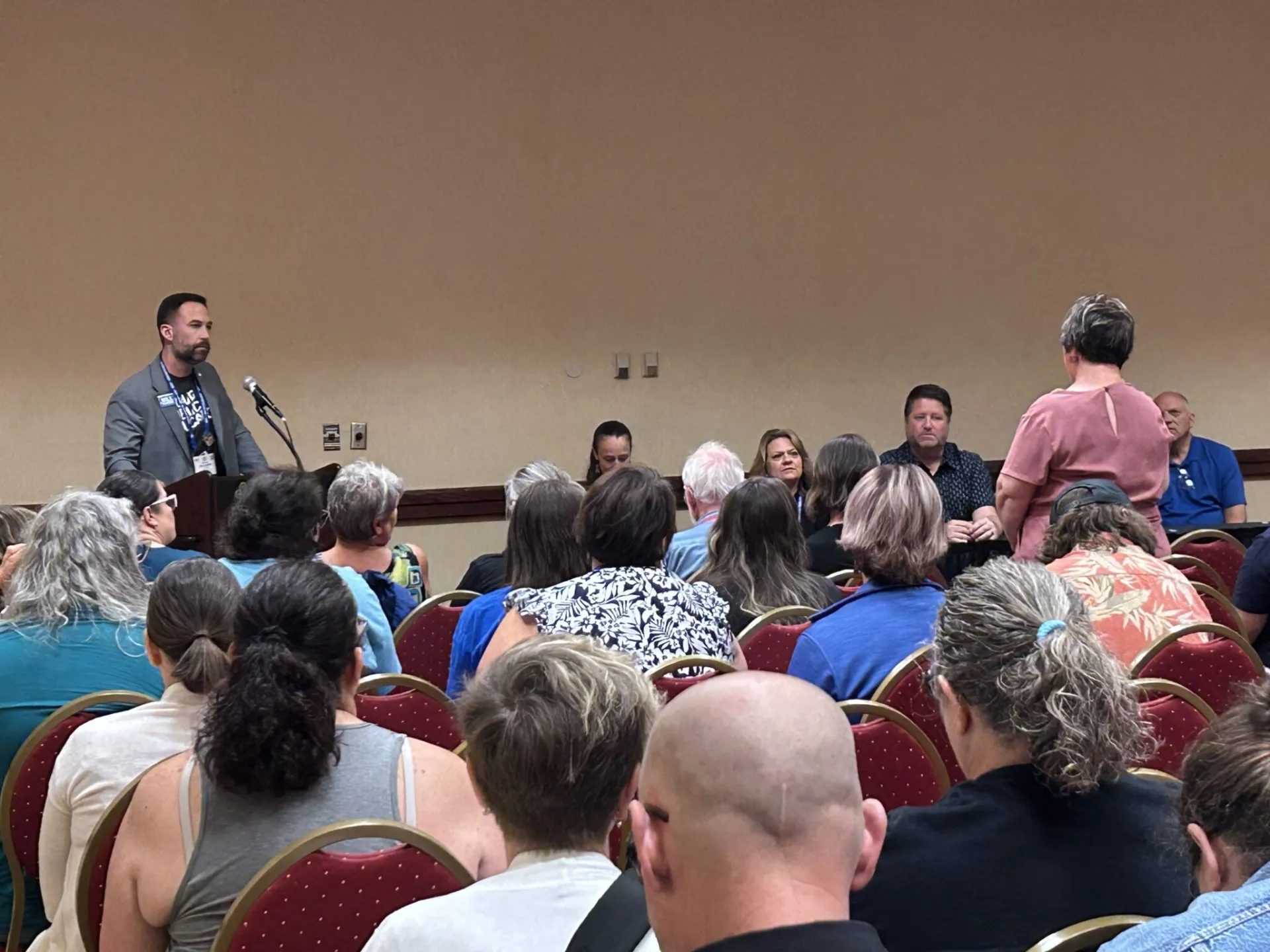 A woman stands up in a crowd and asks a question of a man at a podium