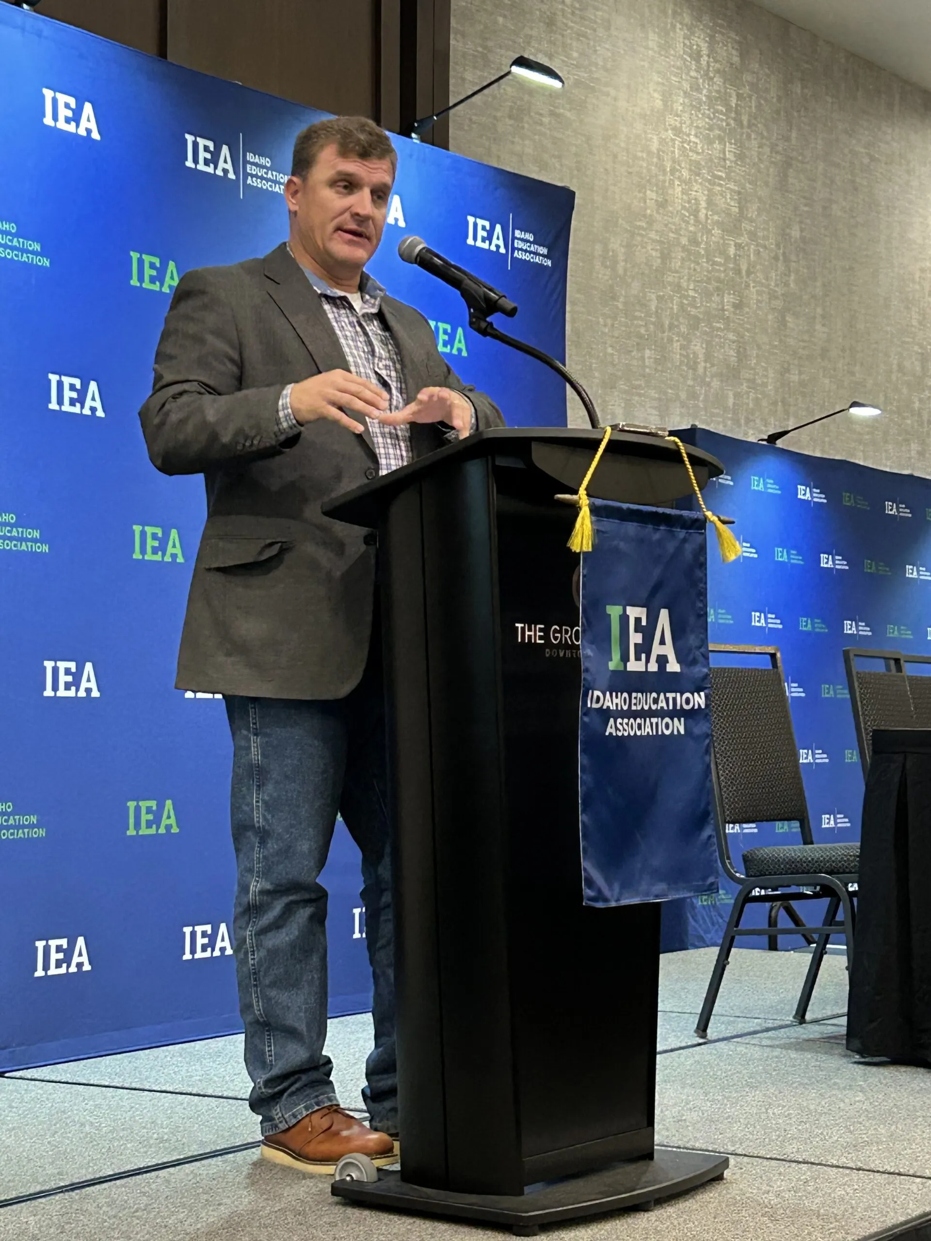 A man in a blazer and jeans at a podium