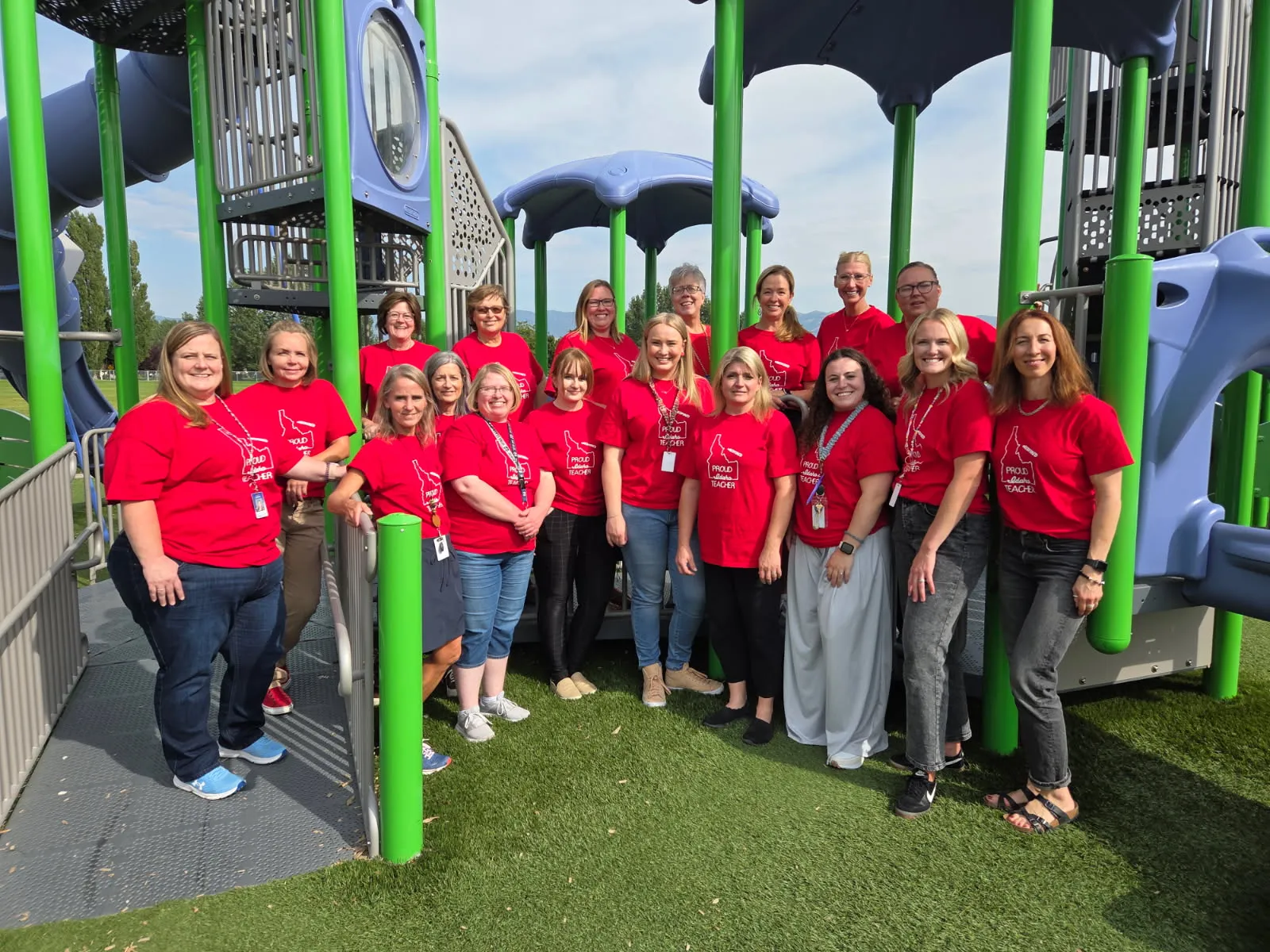 A group of people wearing red shirts poses beneath playground equipment