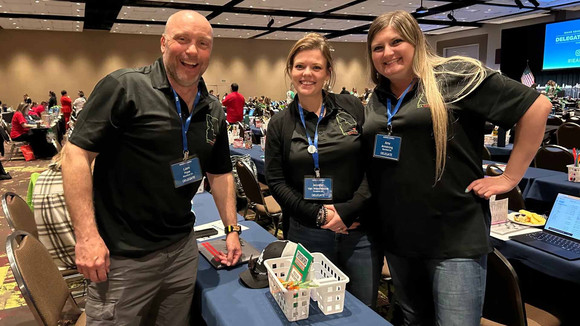 Three smiling people in black shirts in a convention hall