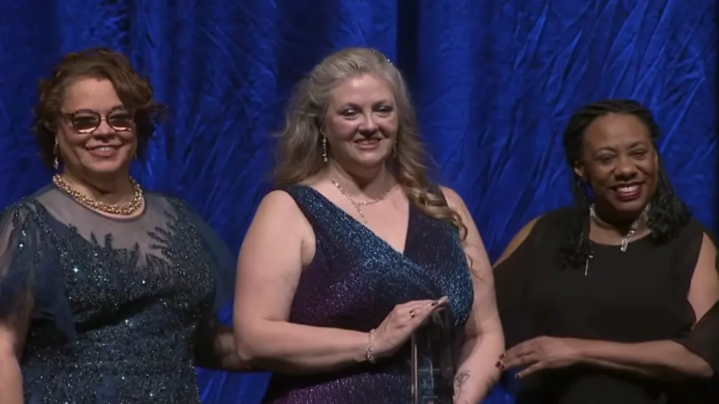 Woman presented with award by two women at gala