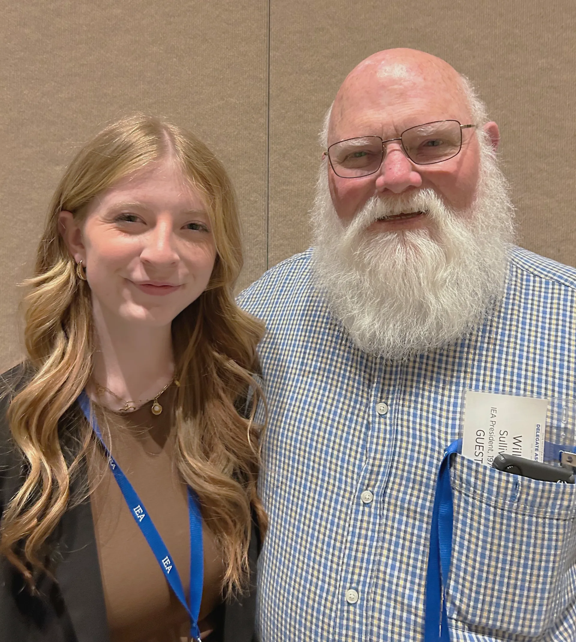 A young woman with blonde hair and an older man with a white beard pose together
