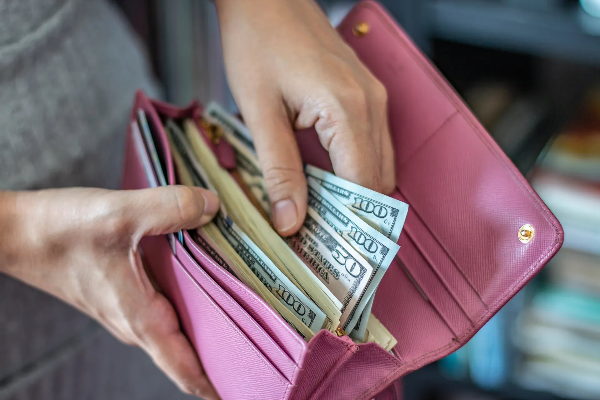 A woman handles money from a pink wallet