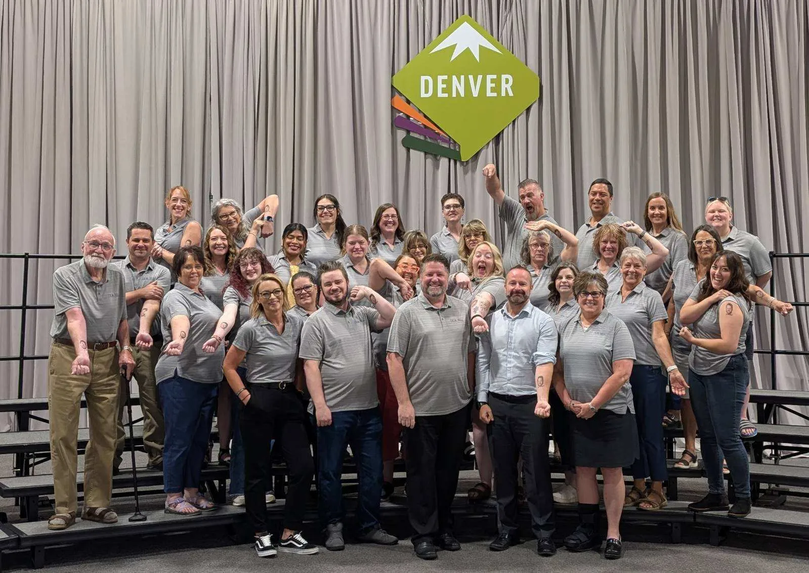A group of people in gray shirts in front of a sign that says Denver