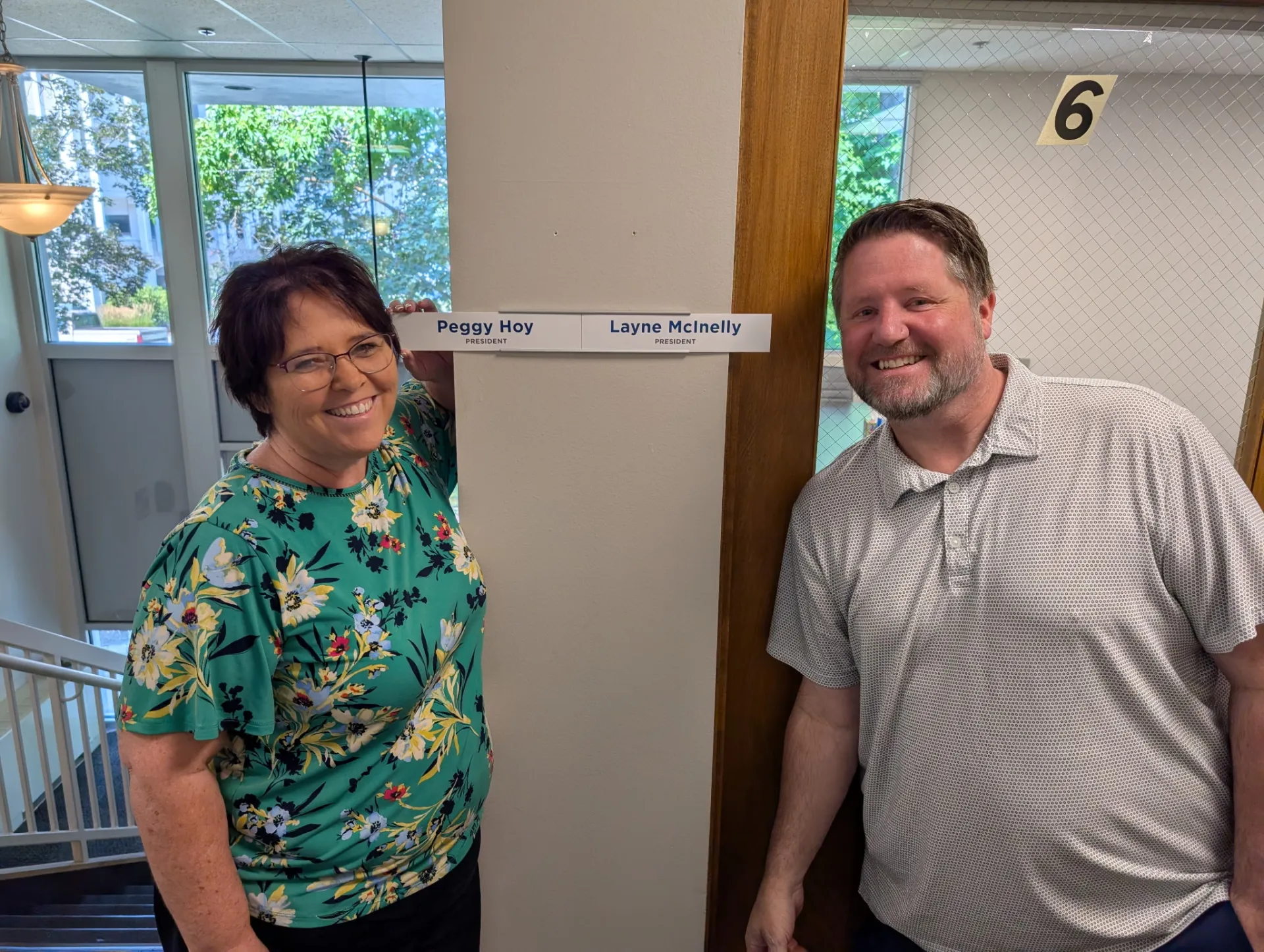 A man and a woman stand next to their office nameplates