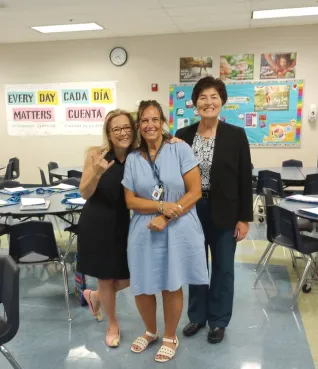 Three women stand in a classroom posing for the camera