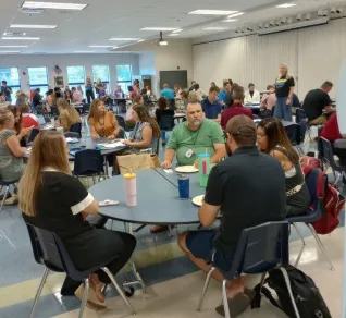 A group of educators seated at round tables in a school cafeteria