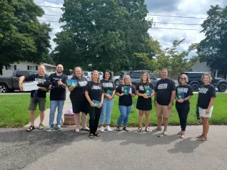 A group of people wearing black shirts and holding brochures smile at the camera