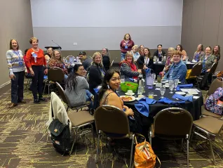 A group of people at tables in a conference room pose for the camera