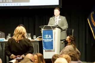 A man at a podium answers a question from a woman in the audience