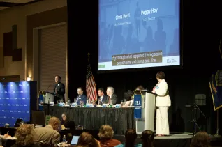 A woman in a white suit speaks at a podium