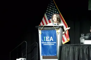 A woman with brown hair speaks at a podium