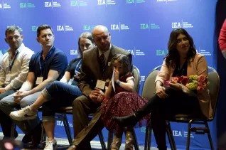 A man in a brown suit and a little girl in a red dress sit among people