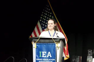 A woman in a white shirt speaks at a podium
