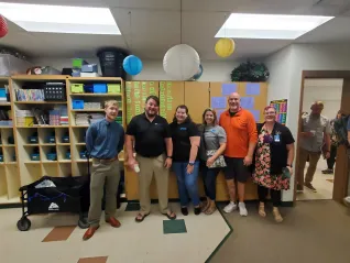Six people in a classroom smile for the camera
