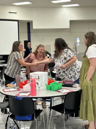 Two women shake hands while another woman laughs and another woman looks on