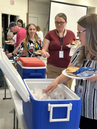 Educators wait in line to grab drinks from a cooler