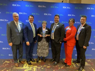 A woman in a black sweater holds an award surrounded by other people