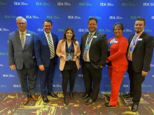 A woman wearing a tan blazer holds an award while flanked by IEA leadership