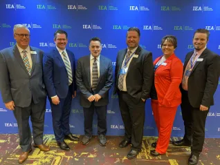 A man in a blue suit surrounded by IEA leadership