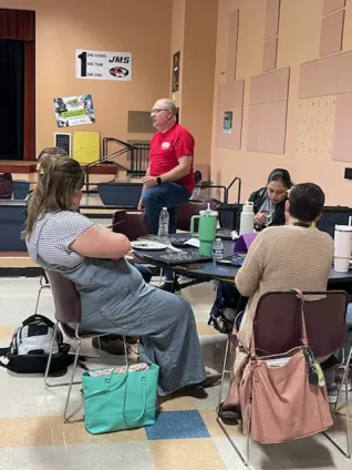 A man speaks to people seated around tables