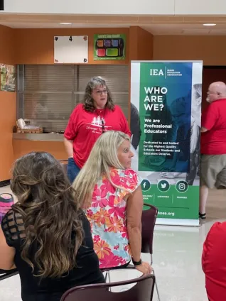 A woman in a red shirt speaks to a group of seated people