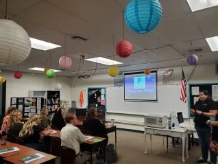 A woman in black speaks to a group of educators seated at desks