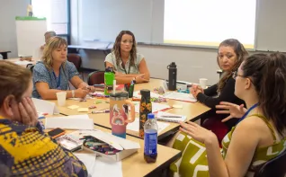 A group of women at a table listen to another woman speaking