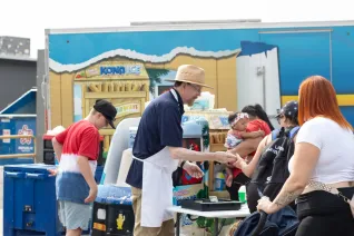 A man wearing an apron and a straw hat passes out food to people in line