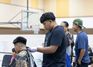 A man gives a haircut to a child in a gymnasium