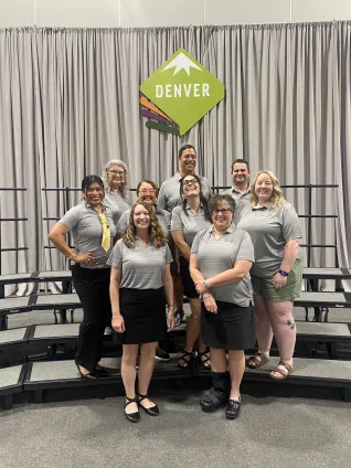 A group of people in gray shirts in front of a sign that says Denver