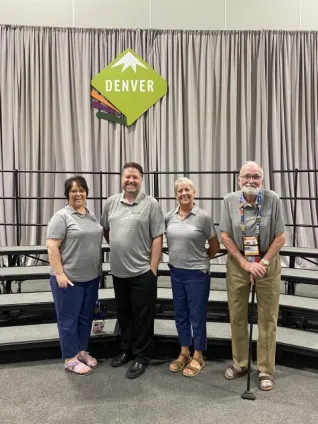 Four people pose in front of a sign that says Denver. 