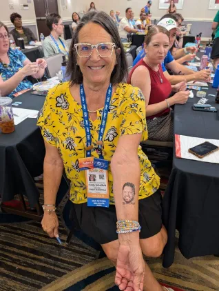 A woman in a yellow shirt shows off a temporary tattoo. 