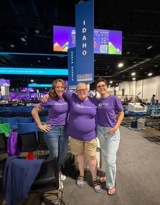 Three women in purple shirts in front of a sign that says Idaho