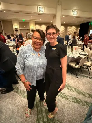 Two women stand with their arms around each other