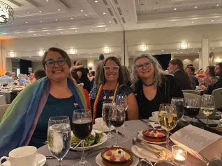 Three women in rainbow gear at a gala dinner
