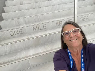 A woman takes a selfie in Denver at the step that says One Mile Above Sea