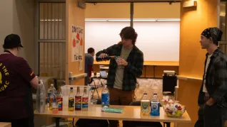 A man pours a beverage while flanked by two people at a table