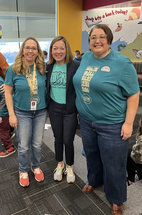 Three women smile at the camera in a classroom