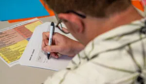 A behind-the-shoulder shot of a man writing on a piece of paper