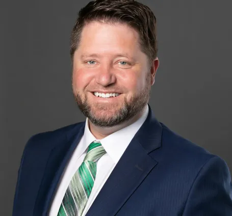 A bearded man wearing a blue blazer, green shirt and white tie