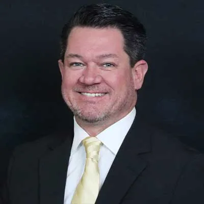 A man with black hair wearing a black suit and a yellow tie