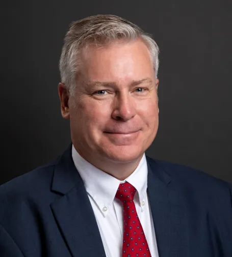 A man in a blue suit jacket and red tie smiles at the camera