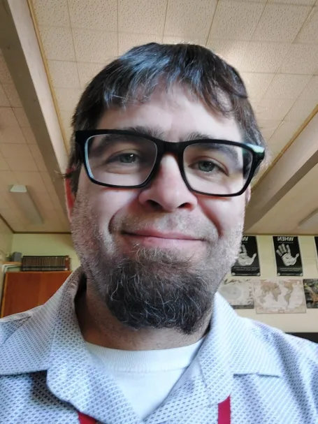 A man with dark hair, a beard and glasses smiling at the camera