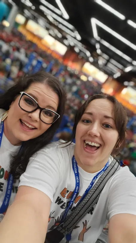 Two women with brown hair stand in an event venue and smile for a selfie