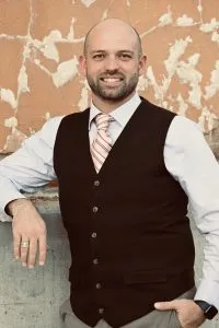 A man wearing a dark vest and striped tie smiles at the camera