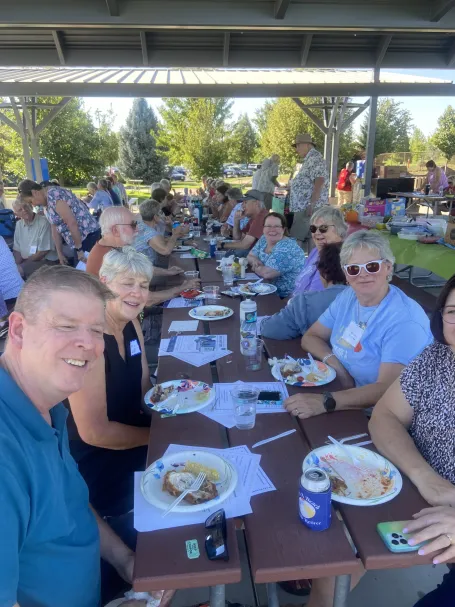 A group of retired people eats around a park picnic table