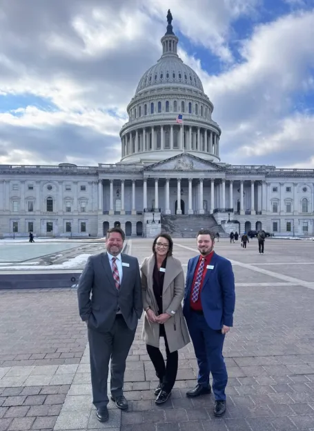 Two men and a woman pose in front of the U.S. Capitol