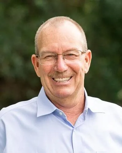 A man with glasses and a pale blue shirt smiles at the camera